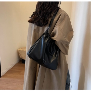 Close-up of a black minimalist leather underarm bag with drawstring folds and thin straps