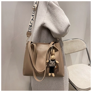 Detail of khaki tote bag with wide geometric strap and cute rabbit charm on a model