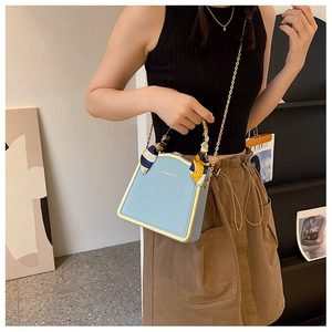 Detail of light blue trapezoid box bag with silk scarf handle and gold chain