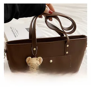 Detail of dark brown leather tote bag with gold rivets and a crochet bear charm