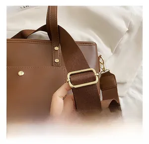 Detail of adjustable fabric shoulder strap with gold buckle on a brown leather tote