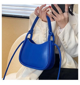 Detail of Klein blue hobo bag with thick handle shown on a model in white blazer