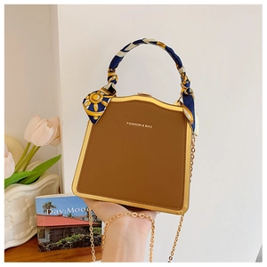 Dettaglio borsa rigida marrone con cornice dorata e manico avvolto da un foulard