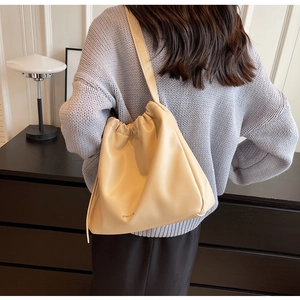 Detail of minimalist beige faux leather shoulder bag worn over a grey knit sweater