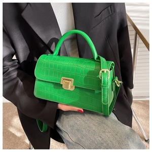 Close-up of vibrant green crocodile pattern bag with golden lock held by a model