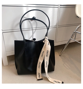 Close-up of black leather tote bag with elegant cream ribbon and brand text detail