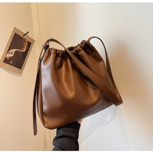 Detail of drawstring closure and brand logo on brown matte leather bucket bag