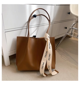 Detailed view of large brown tote bag with decorative vertical stitching and ribbon charm