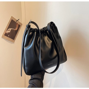 Detail of a black matte soft leather drawstring bucket bag with minimalist brand logo
