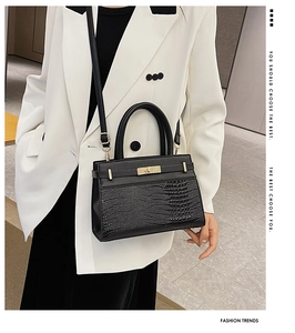 Detail of black faux crocodile leather crossbody bag with elegant gold twist lock and handle