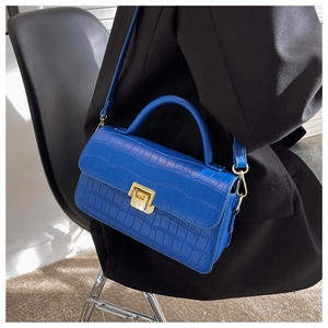 Detail view of royal blue crocodile embossed handbag with gold metal clasp on black blazer