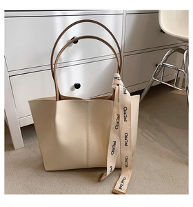 Detail of minimalist cream tote bag with contrast dark brown handles and branded ribbon trim
