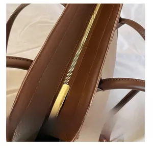 Detailed close-up of the smooth gold metal zipper on a premium brown leather tote bag