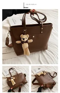 Detail view of brown PU leather tote bag featuring golden rivets and knitted bear charm
