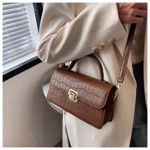 Detail of crocodile embossed texture on brown handbag with golden metal twist lock closure