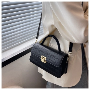 Detail of black faux crocodile skin handbag with golden lock and adjustable strap
