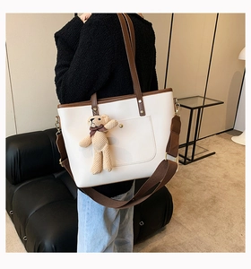 Detail shot of stylish contrast tote bag featuring plush bear charm and brown woven strap