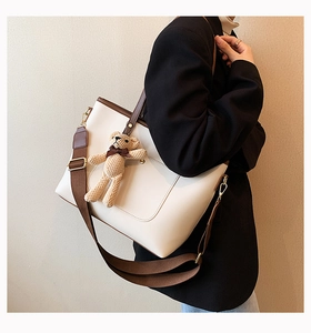 Detail view of white leather tote bag with brown trim and cute knit bear pendant