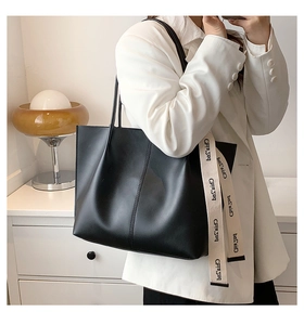 Close-up of a black leather tote bag with unique beige long logo ribbon handle detail