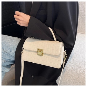Detail of cream faux crocodile texture handbag with gold metal lock and leather strap