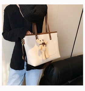 Detail of off-white tote bag with brown straps and a cute knitted bear charm accessory