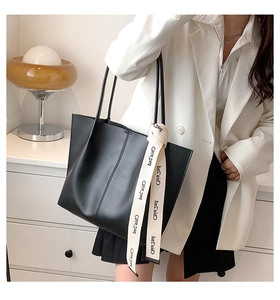 Close-up of black large capacity tote bag with decorative lettered ribbon on a model