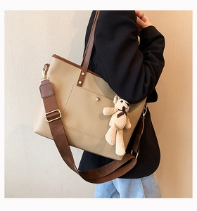 Detail of a beige tote bag with brown handles and a cute plush teddy bear charm