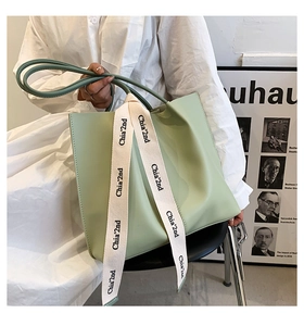 Close-up of mint green leather tote bag with stylish printed ribbon and long handles