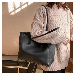Detail view of large black pebble leather tote bag worn by a model in a natural setting