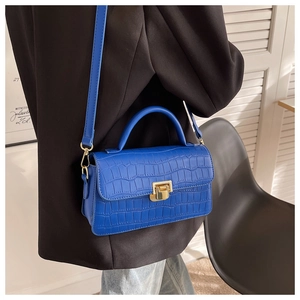 Close-up of blue crocodile texture handbag with gold metal lock on a black suit