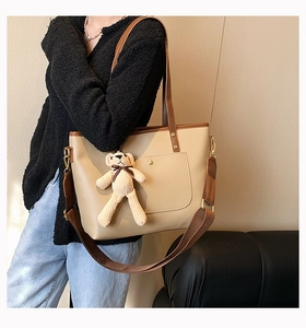 Detail view of large beige tote bag with brown handles and a cute bear charm accessory