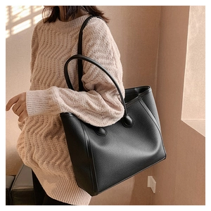 Close-up of black pebble leather tote bag featuring slim cylindrical handles and texture