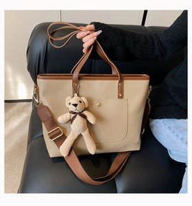 Detail of minimalist beige tote bag with brown handles and a cute bear bag charm