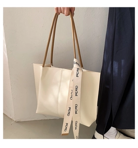 Detail of off-white tote bag featuring slim brown straps and brand logo ribbon