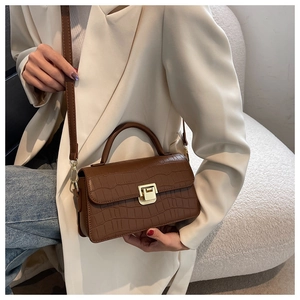 Detailed view of brown crocodile texture leather handbag with gold metal clasp and strap