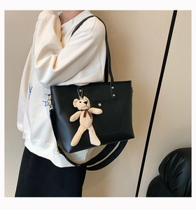 Modern black faux leather tote bag on shoulder with a cute plush bear charm detail
