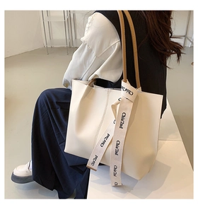 Detail of a large beige tote bag featuring a brown leather strap and knotted printed ribbon