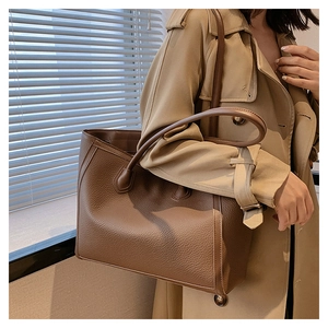 Detailed close-up of brown pebbled leather tote bag with sturdy handles and neat stitching