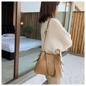 Detail of a khaki leather bucket bag with adjustable strap and golden logo on side