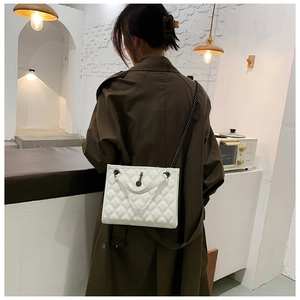 White quilted chain shoulder bag shown on model with olive trench coat in cozy indoor setting