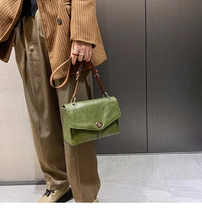 Detail of green oil wax leather handbag with bronze twist lock and slim brown shoulder strap