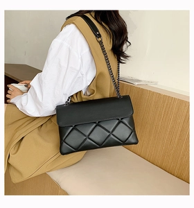 Detail of a black quilted leather chain bag worn with a white shirt and brown vest