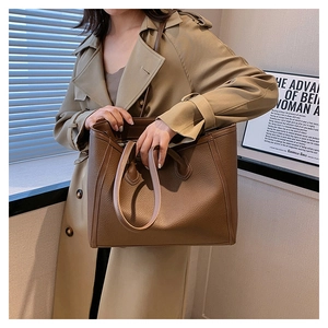 Detail of a large brown leather tote bag with lychee texture held by a model in a trench coat