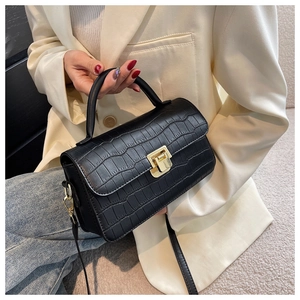 Close-up of black crocodile-textured small square handbag with golden clasp detail