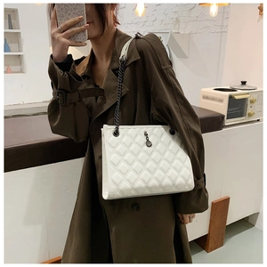 Close-up of white quilted shoulder bag with dark metal chain strap and round pendant charm