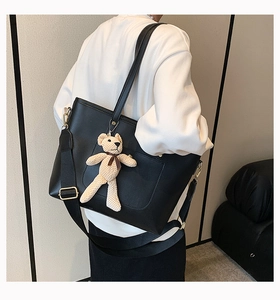 Detail of black faux leather tote bag with plush bear charm and wide nylon strap