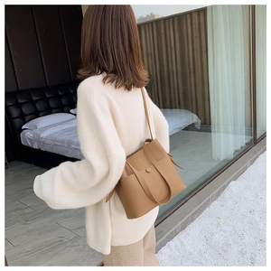 Close-up of brown leather bucket bag with gold Classy Bag logo on a female model