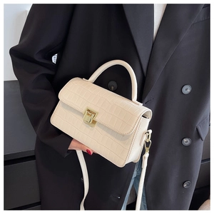 Detail of creamy white crocodile embossed bag with a gold metal lock and leather handle