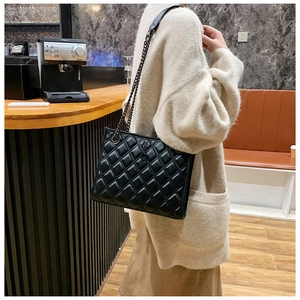 Close-up of quilted black leather texture and metal chain strap on a shoulder bag