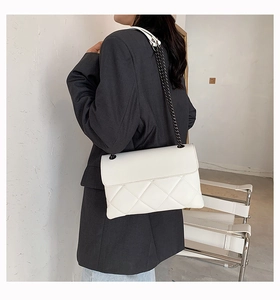 Detail view of white quilted chain bag worn by a model against a minimalist background